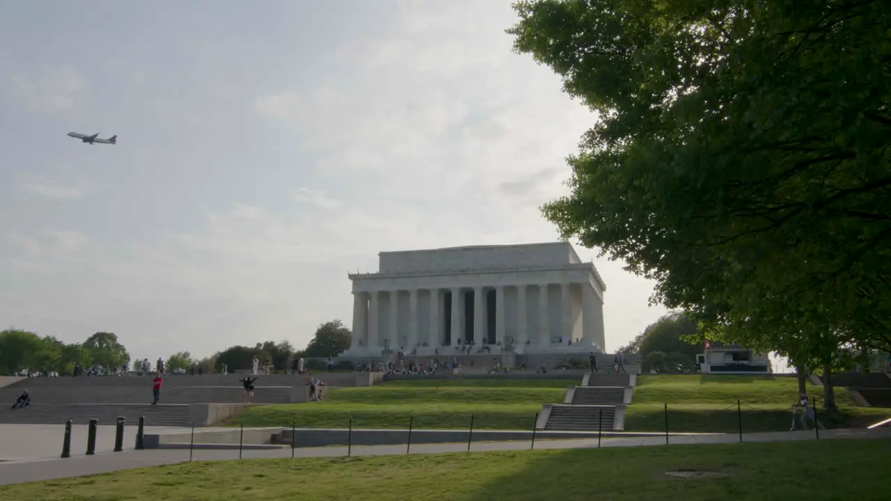 The Lincoln Memorial stands on a sunny spring day as a plane flies overhead and pedestrians enjoy the surroundings