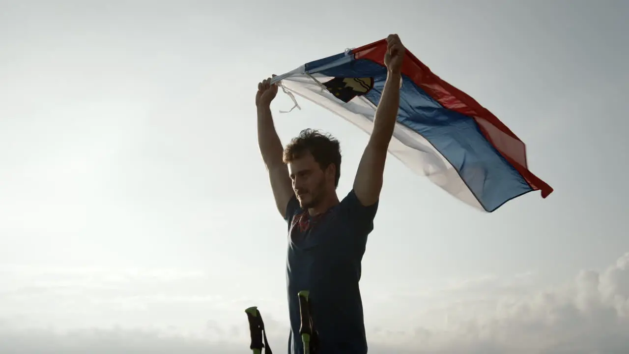 A young hiker holding in his hands a slovenian flag above his head and let it flutter in the wind camera cicling arond him