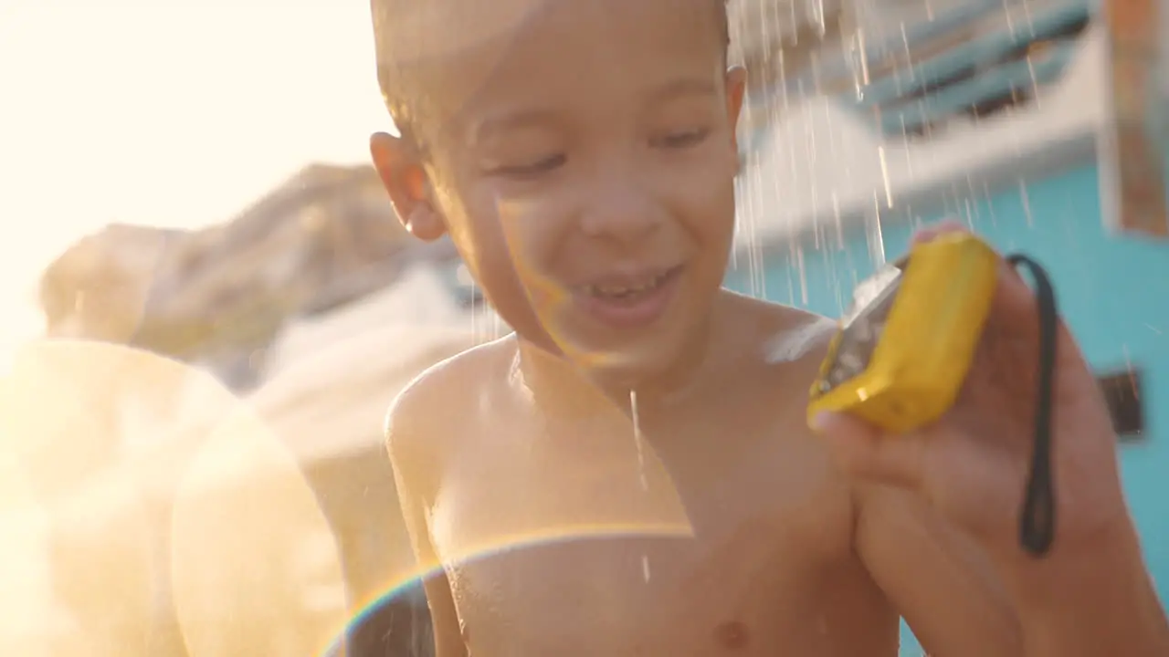 Child taking beach shower and watching photos on waterproof camera