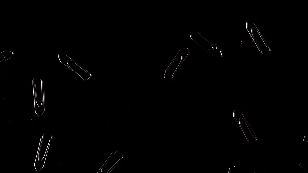 Slow motion shot of paperclips falling down in a studio setup with a isolated black background