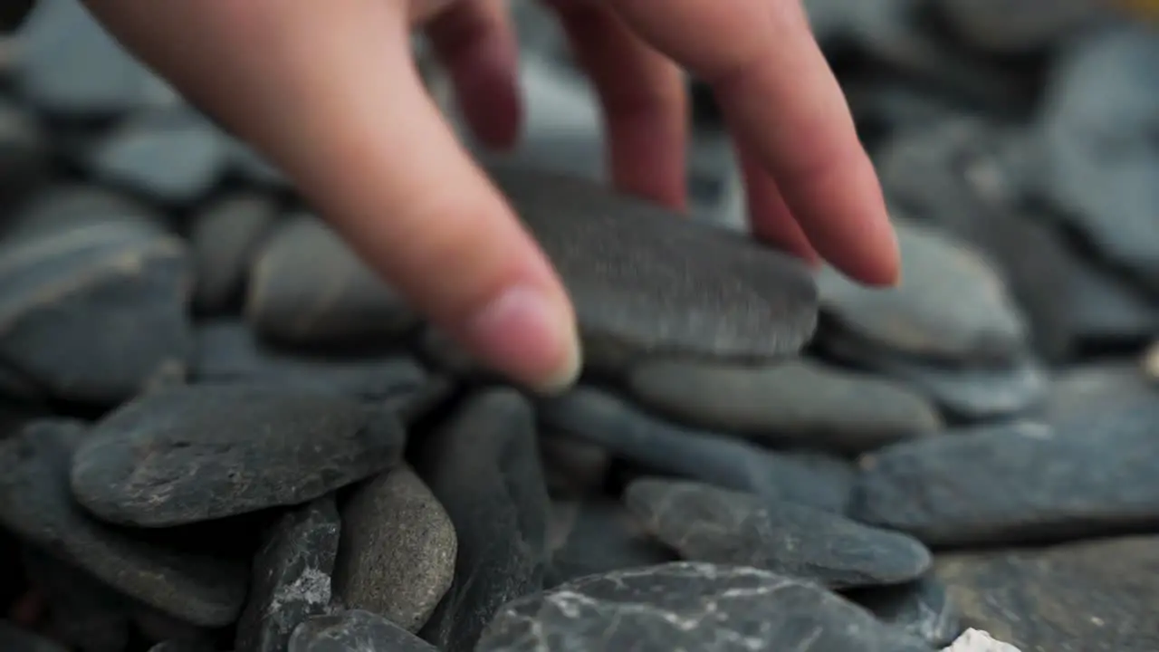 Female hand picking up flat rock on beach slow motion close up