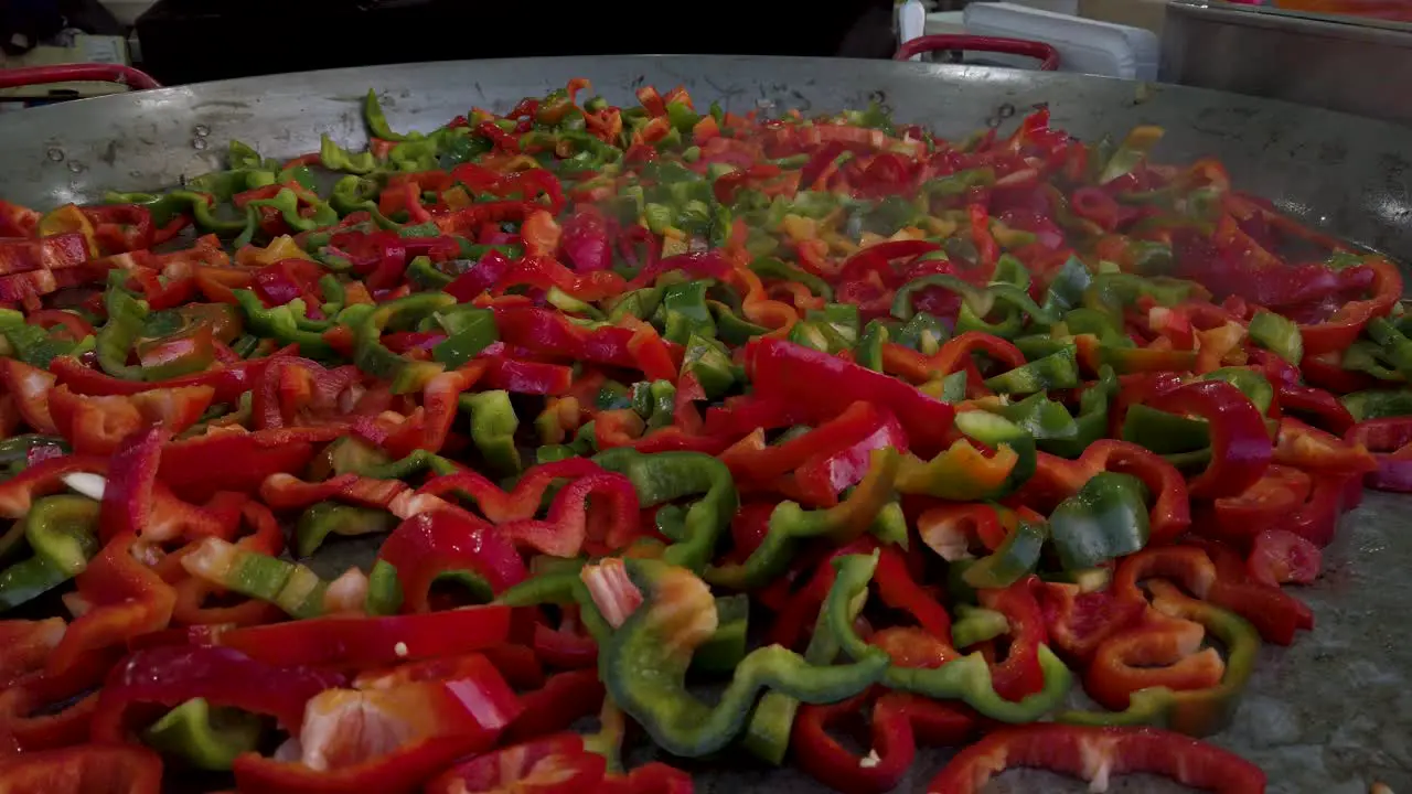 Red and Green sliced peppers on huge street vendor frying pan Closeup Push In