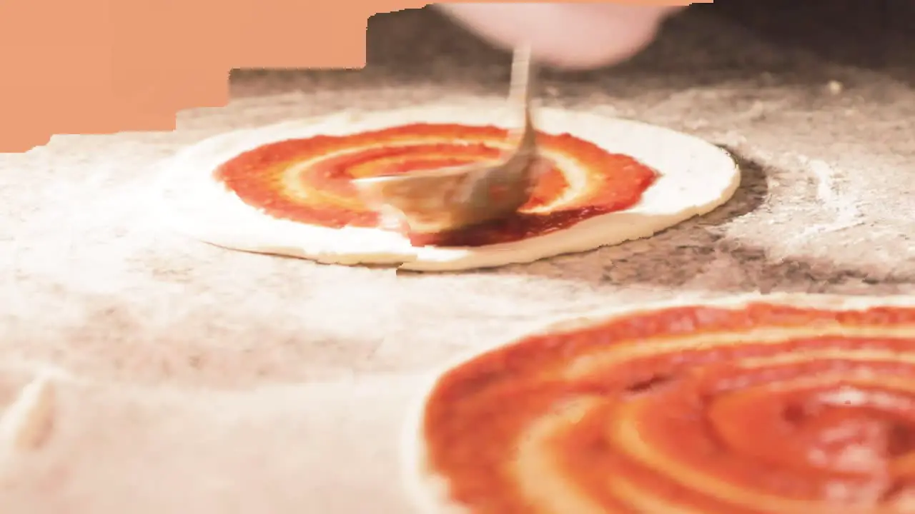 Cook preparing pizza dough with tomato sauce for the oven with bright light in kitchen