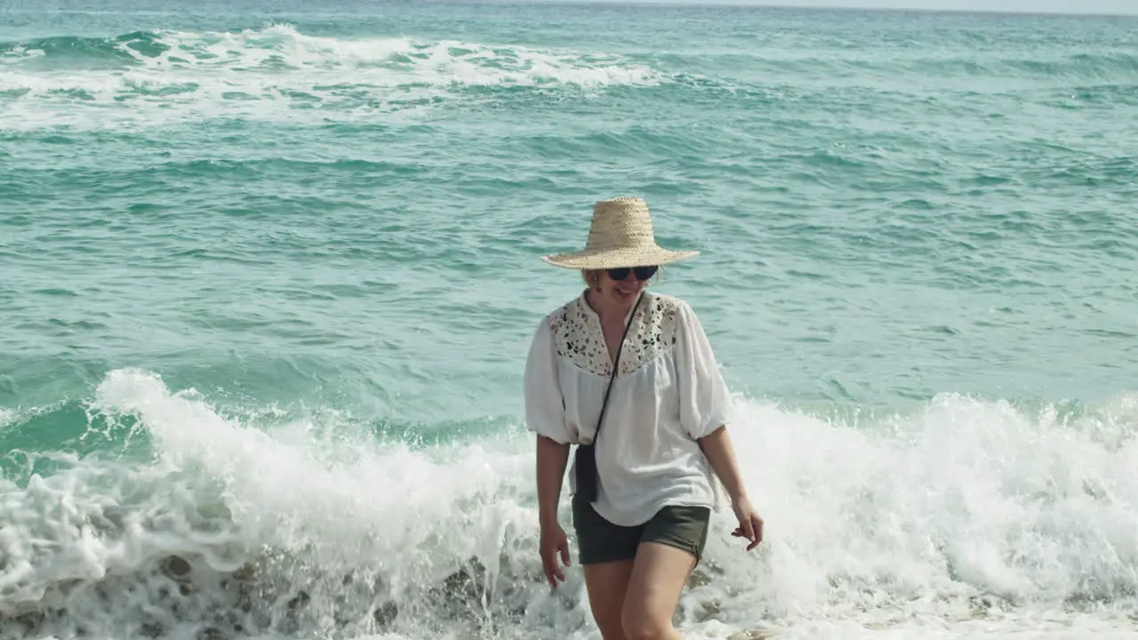 Woman strolls the beach as summer waves splash her legs slow motion