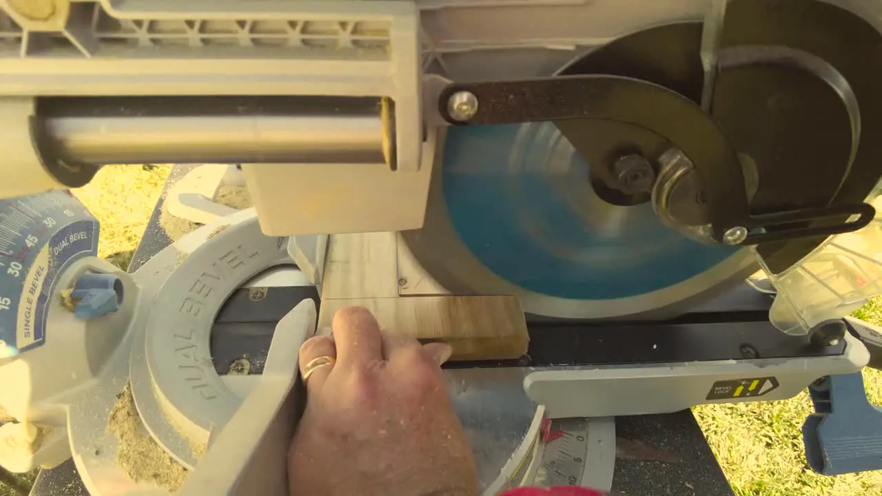 Man using miter saw to cut through wood for a project on a sunny day