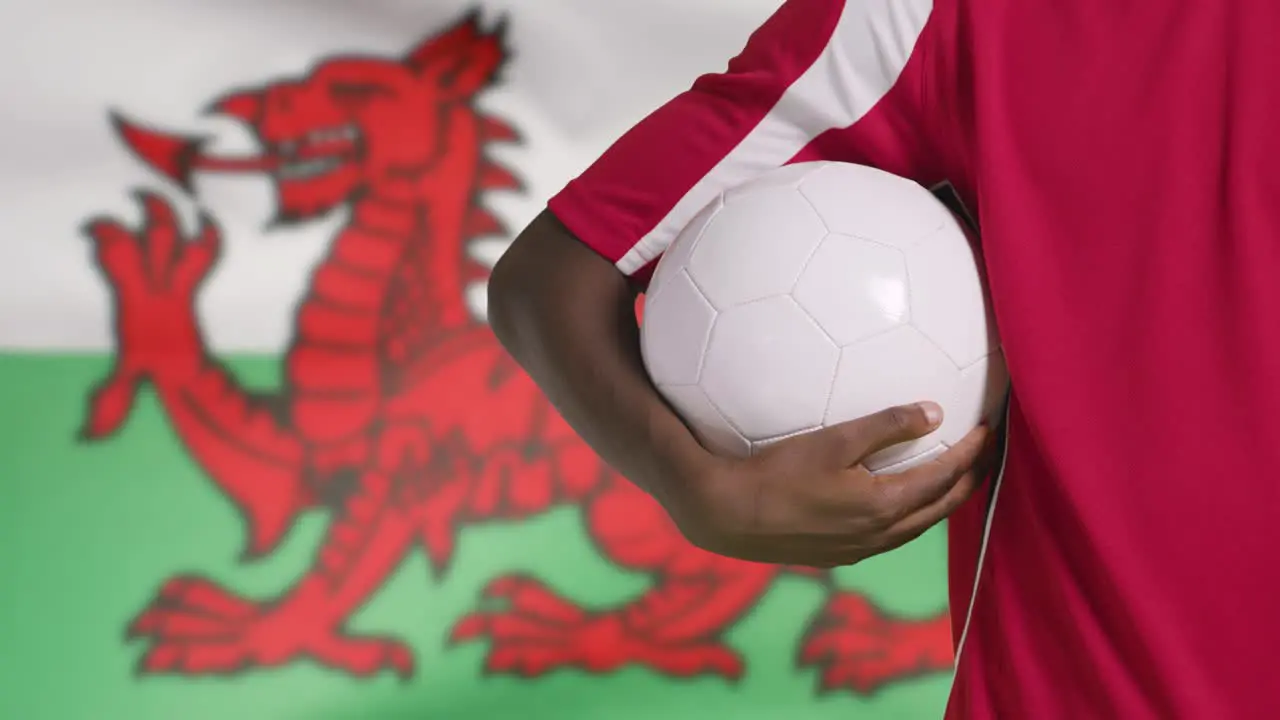 Young Footballer Walking Holding Football In Front of Wales Flag