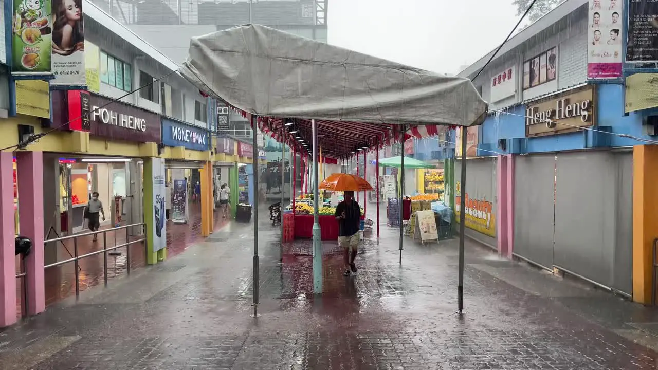 Man carries an orange umbrella and walks under the tentage in Ang Mo Kio the rainy season in Singapore