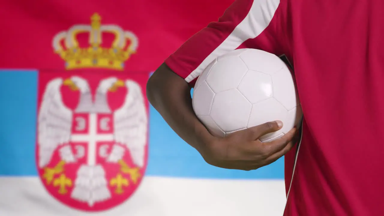 Young Footballer Walking Holding Football In Front of Serbia Flag