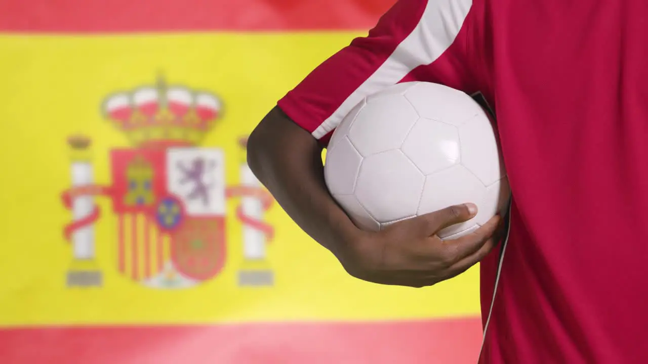 Young Footballer Walking Holding Football In Front of Spain Flag 01