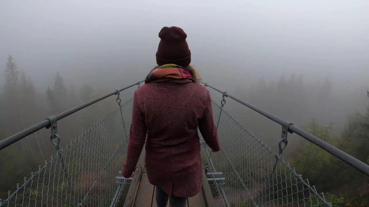 A young woman crossing a bridge above a small foggy valley