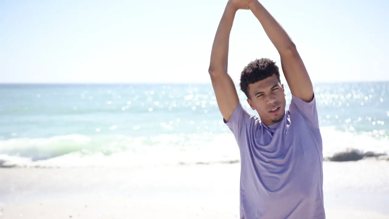 Young biracial man stretches his arms on a sunny beach