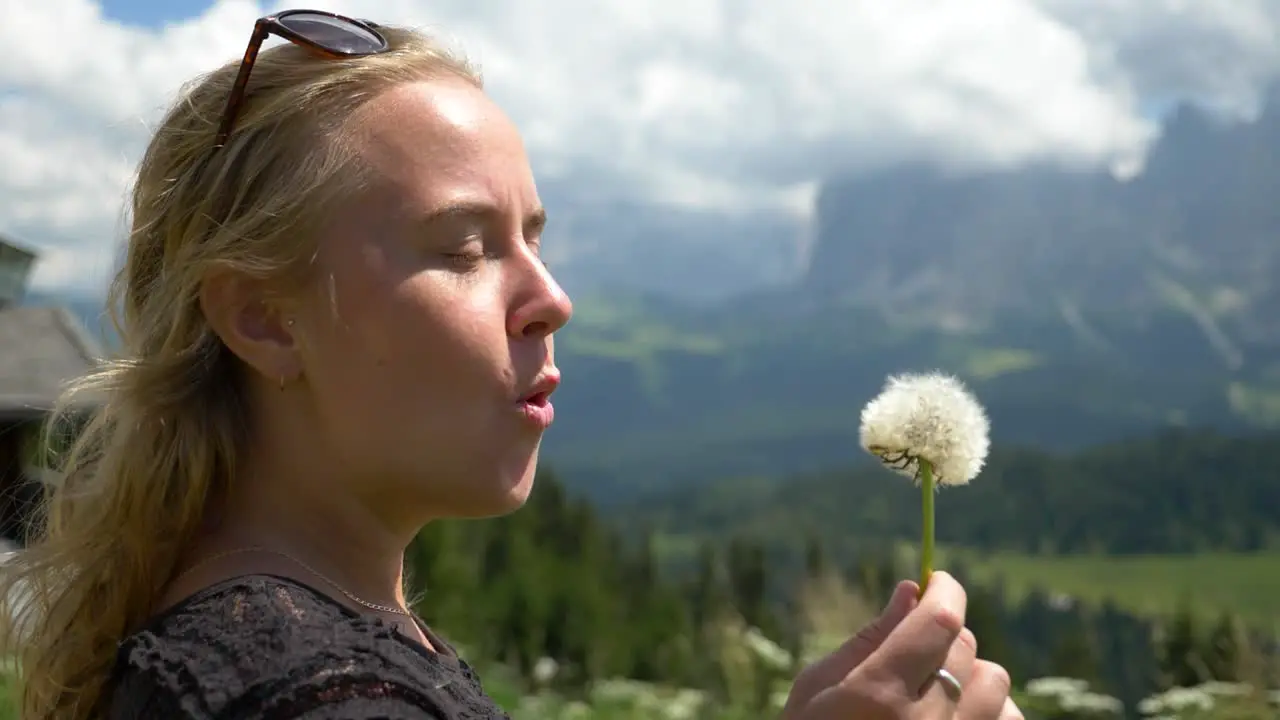 Super slow Mo of a Caucasian female model blowing a dandelion flower in against the wind Seiser Alm Val Gardena South Tirol