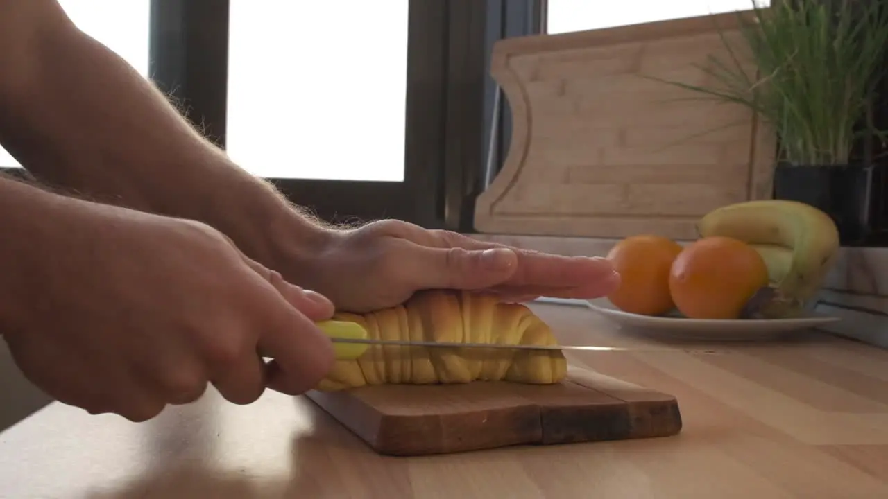 Man Cutting Croissant Bread With Knife On Wooden Board In The Kitchen For Breakfast