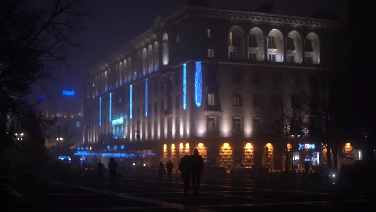 Blue and purple light up an urban building as people walk towards club at night