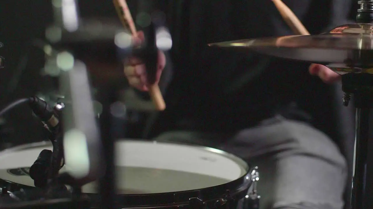 Smooth slow motion of a drum set being played in front of a dark background while camera makes a panning gimbal movement