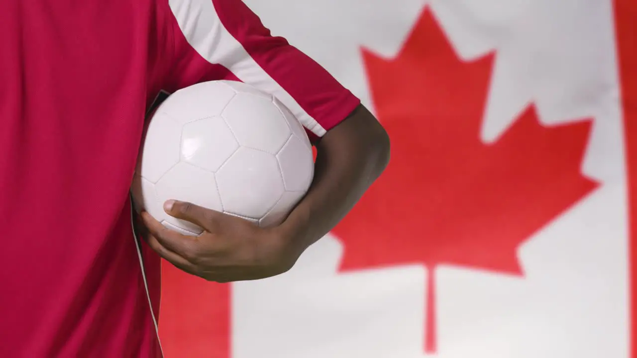 Young Footballer Walking Holding Football In Front of Canada Flag