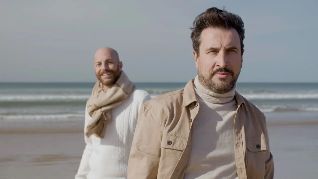 Front View Of A Happy Gay Couple Looking And Smiling At The Camera While Standing On The Beach