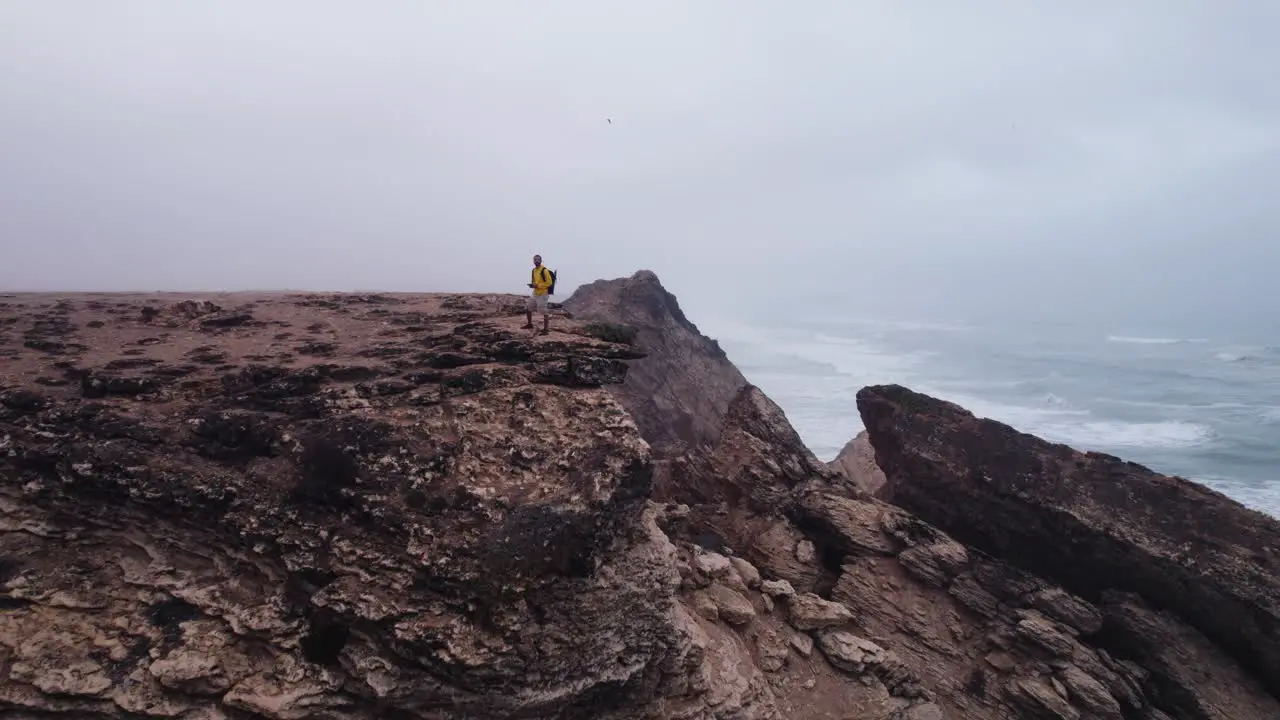 Man standing on a cliff in the sea in a foggy weather drone clip