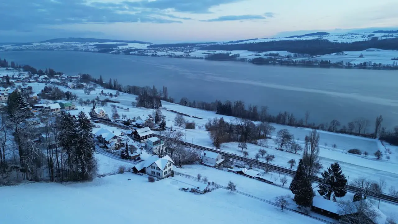 Wintry morning with a drone flying over a snow-covered landscape with a lake in Switzerland trees and hills in the background