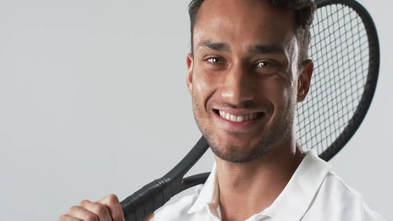 Young biracial man poses with a tennis racket