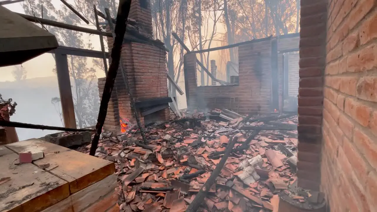 Smoke is coming out from the debris burnt wood and tiles of a house that has burnt to the ground by a wildfire