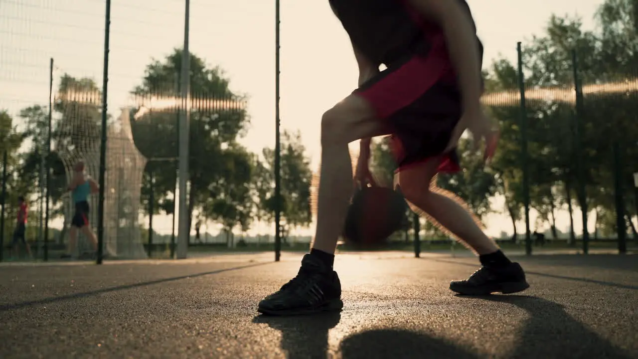 Close Up Of A Male Basketball Player Dribbling The Ball Between His Legs In An Outdoor Court At Sunset