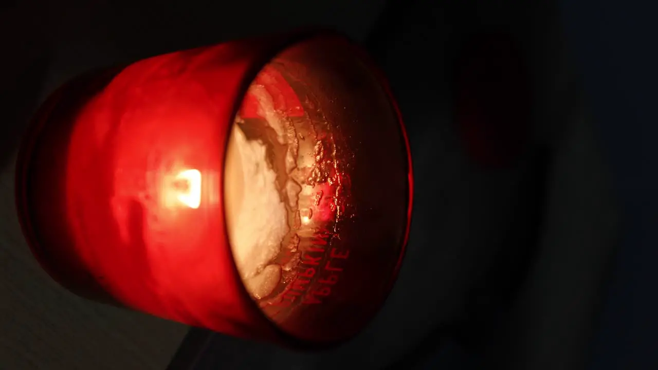 Static shot of a bright red candle glowing and burning out as wax gets low with the words "pumpkin apple" visible through the glow of the glass and a lighter and candle cap visible in the blurred back