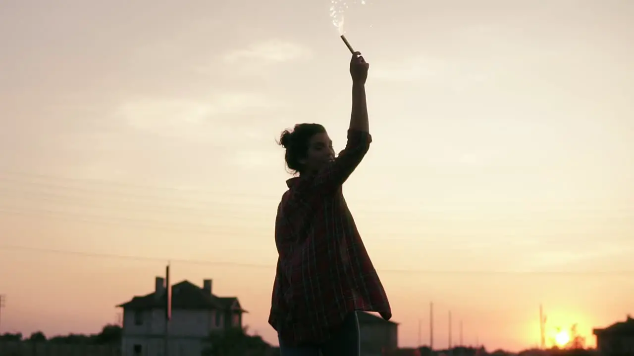 Young Woman Standing With Firework Candles During Sunset And Looking In The Camera