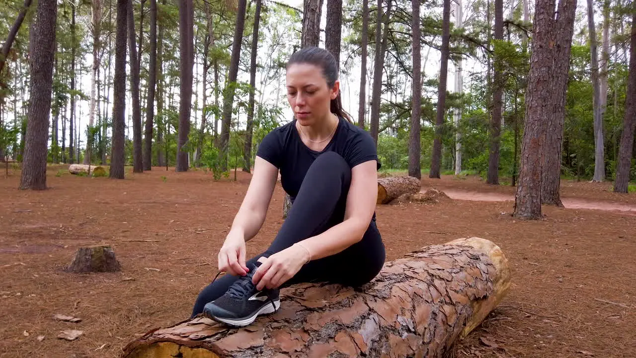 Caucasian blond woman sitting on a fallen tree in the forest tying running shoes