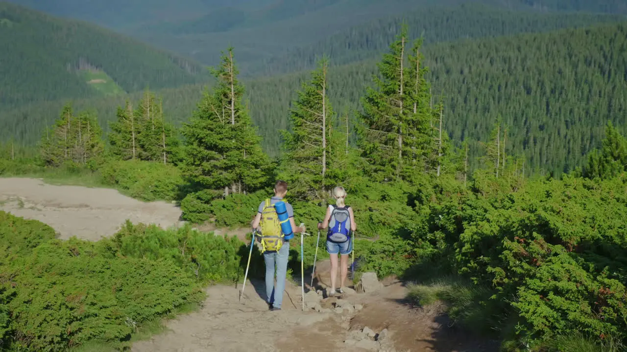 Tourists A Man And A Woman With Backpacks On Their Backs Descend Down The Mountain Trail 4K Video