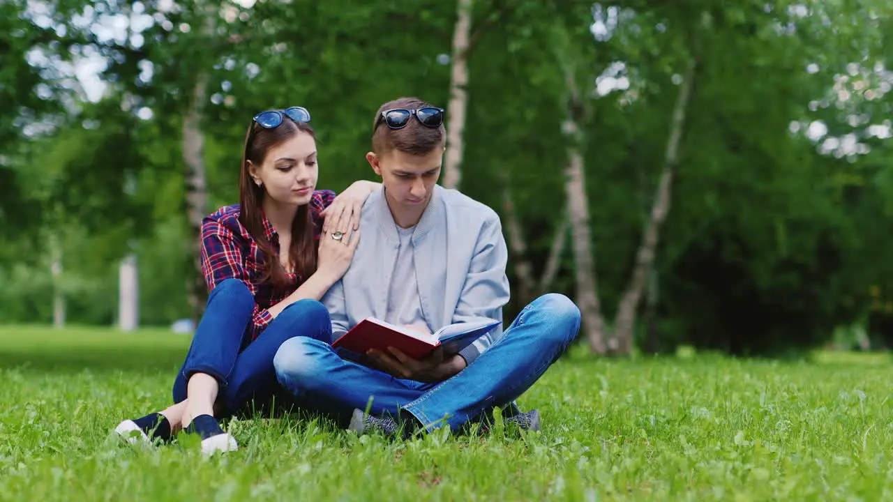 Young Man And A Woman Reading A Book In The Park They Sit On A Green Lawn Hd Video