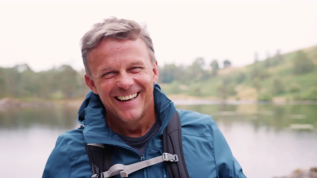 Middle aged man standing on a camping holiday standing by a lake laughing close up Lake District UK