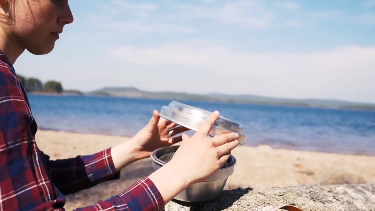 Swedish girl takes of lid of a Trangia portable stove to cook at the lake