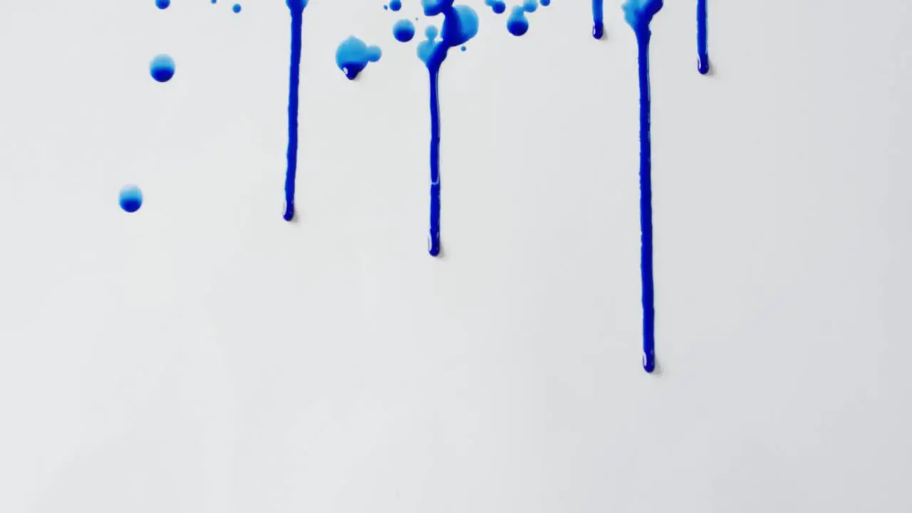 Close up of blue paint shapes on white background with copy space slow motion