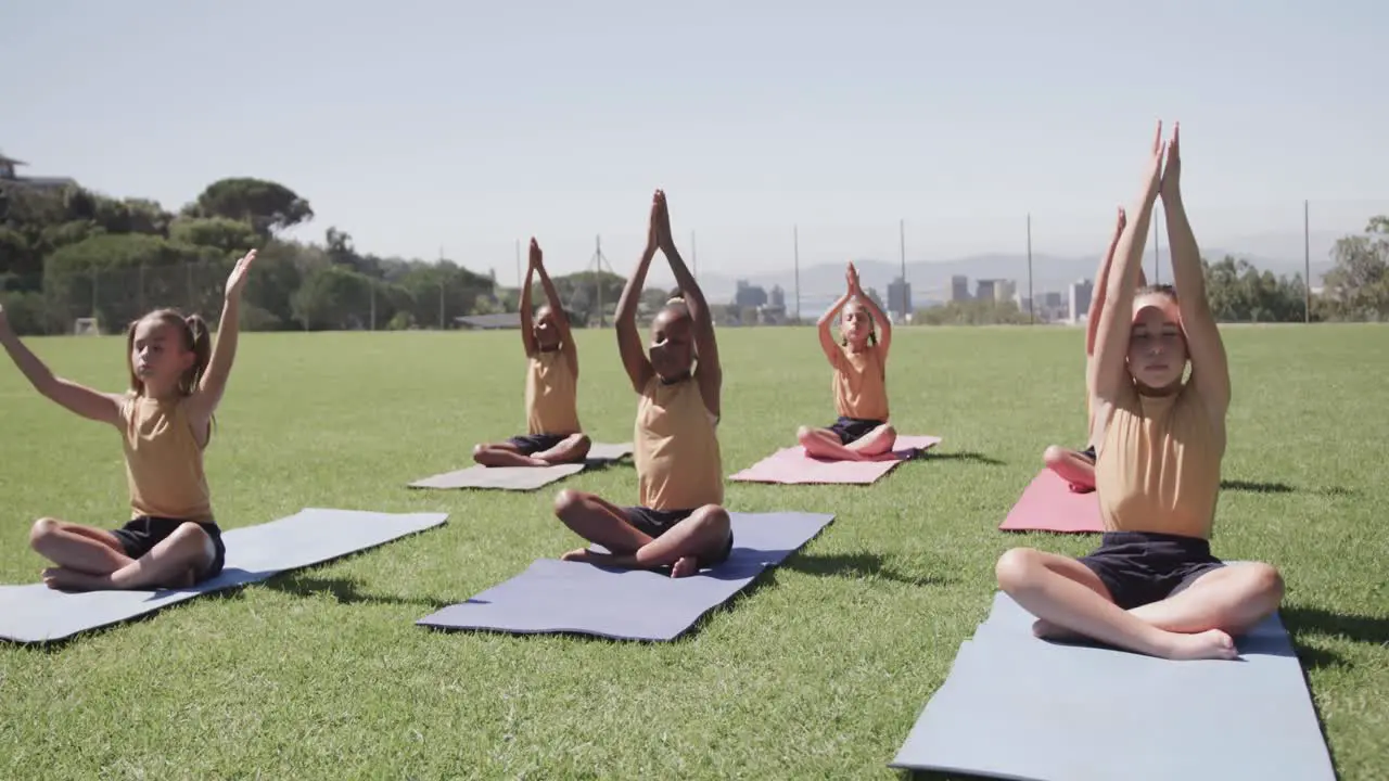 Focused diverse schoolgirls practicing yoga and meditating at stadium in slow motion