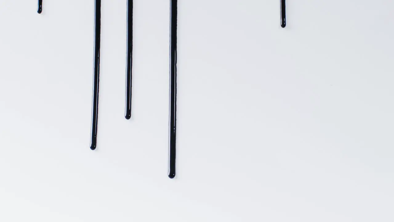 Close up of black paint shapes on white background with copy space slow motion