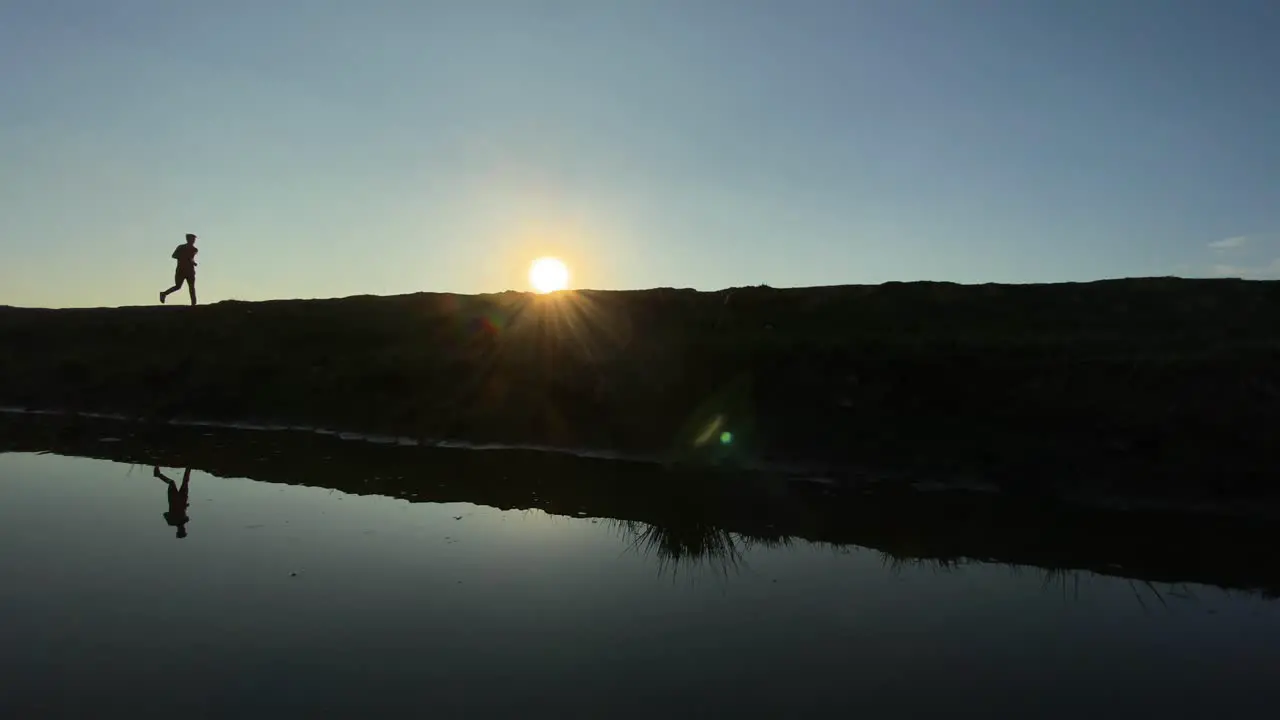 Skinny young man running at morning sunrise hour beside a lake