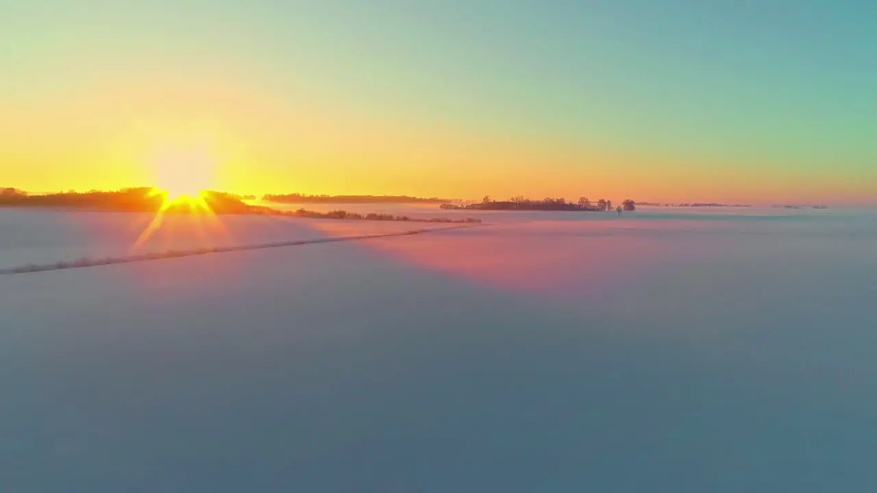 Glowing golden sunset on the horizon of an empty snowy landscape of rural farmland fields aerial view