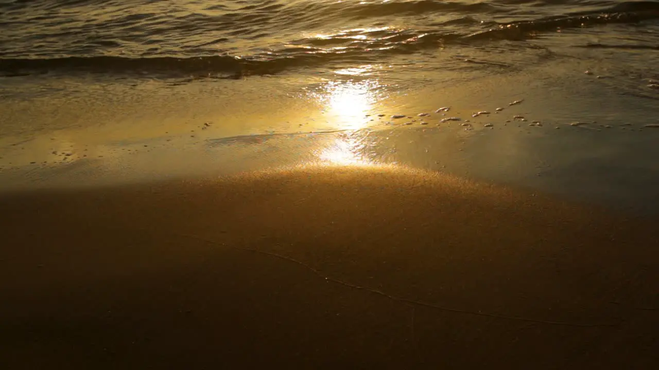 Peaceful waves rolling over smooth wet sand during the sunset -close up