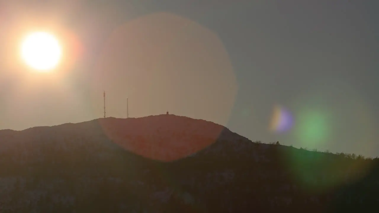 Tele shot of sun going down along a mountain ridge with a beautiful lens flare before disappearing