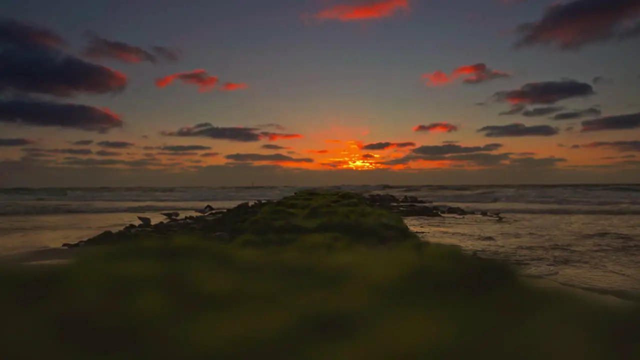 Waves are coming next to a groyne at a beach at sunset time red glowing twilight at the horizon