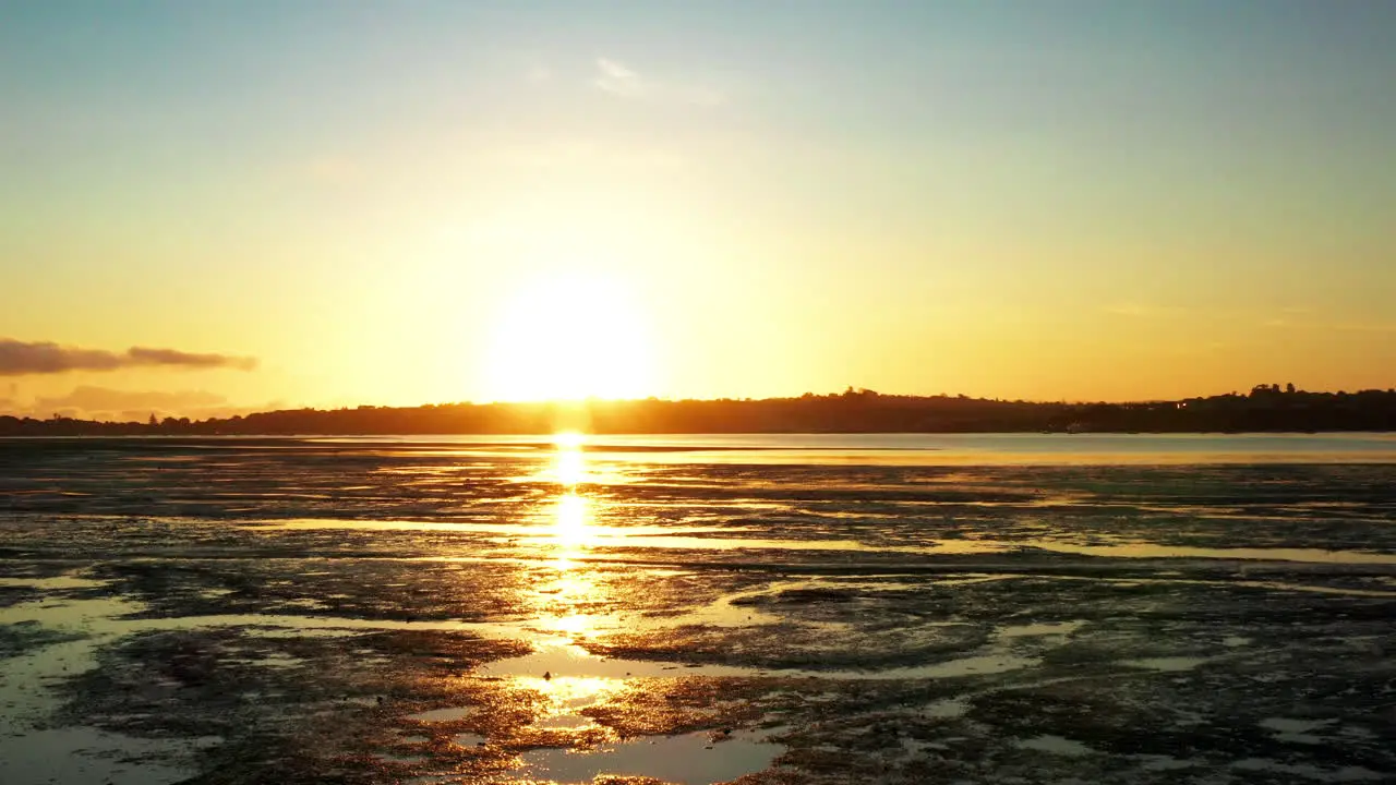 Rear aerial sunset above shallows and low coastline tide near Auckland