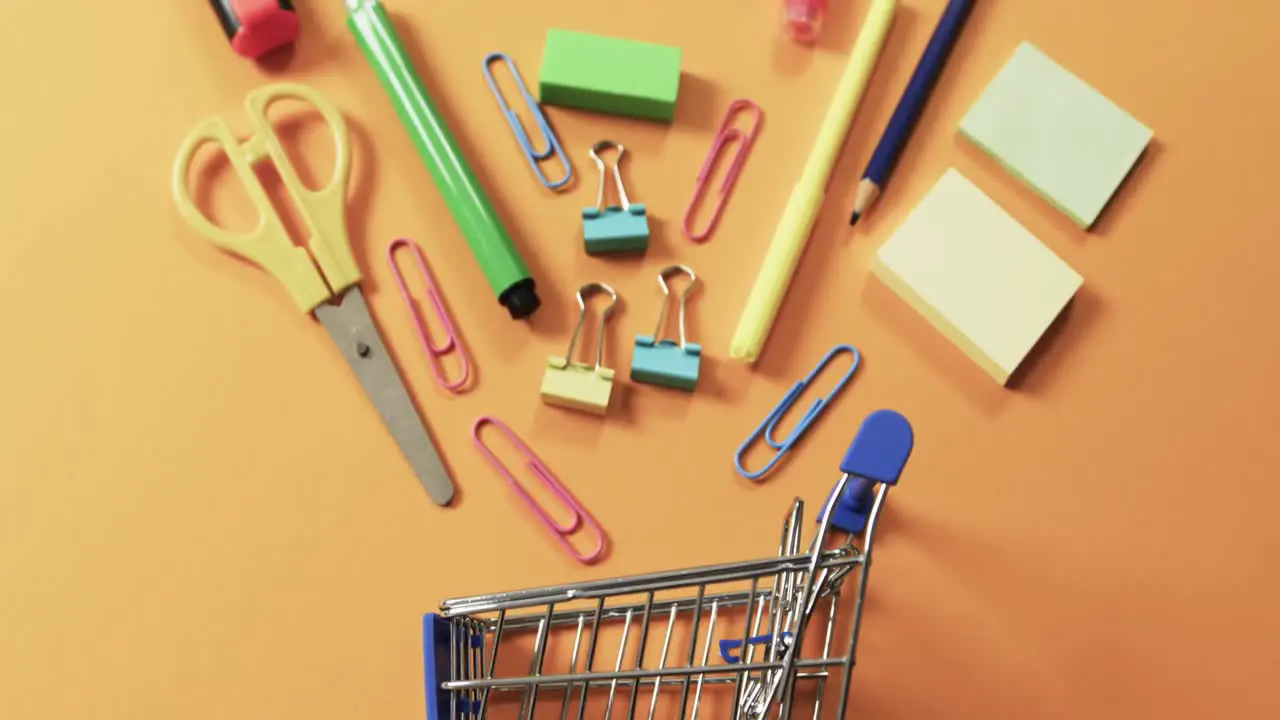 Overhead view of shopping trolley and school items on orange background