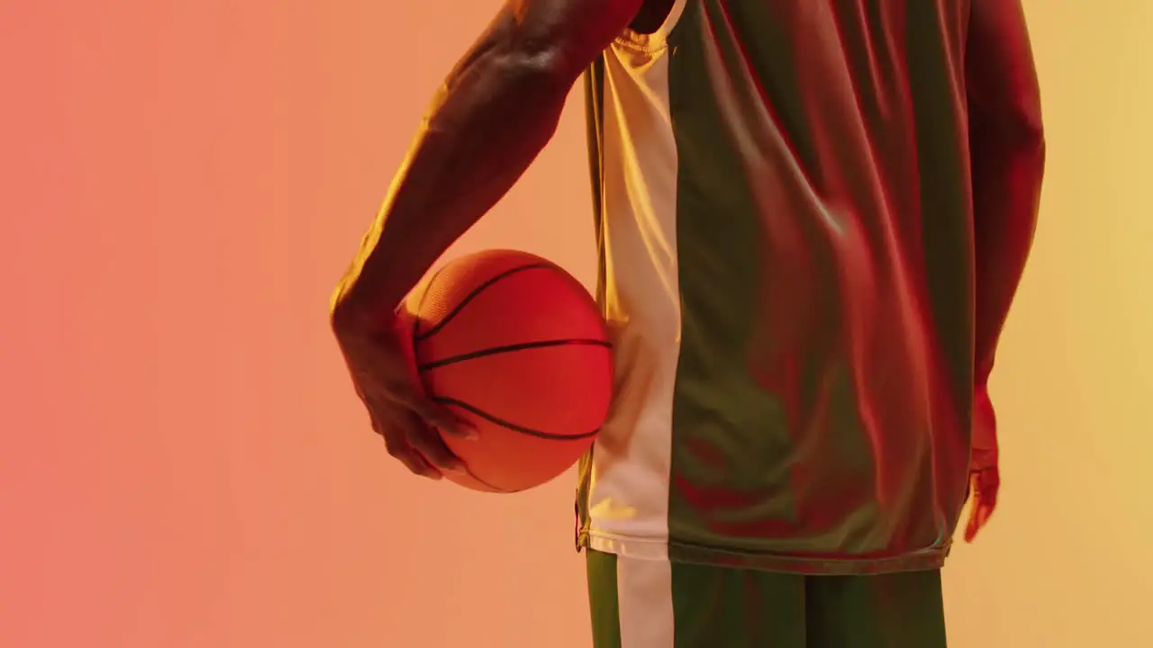 Video of rear view of african american male basketball player holding ball on orange background