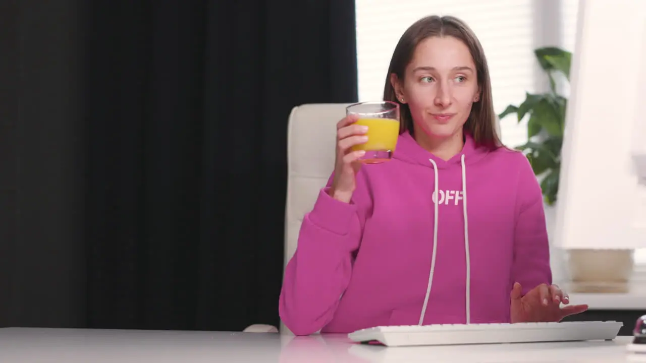 Young Woman Drinking An Healthy Orange Juice While Using Desktop Computer At Office 1