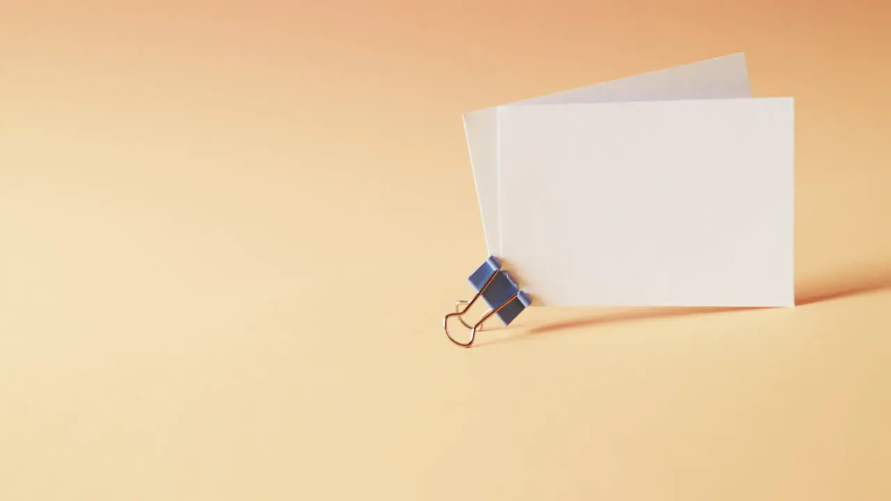 Two blank white business cards with bulldog clip on orange background copy space slow motion