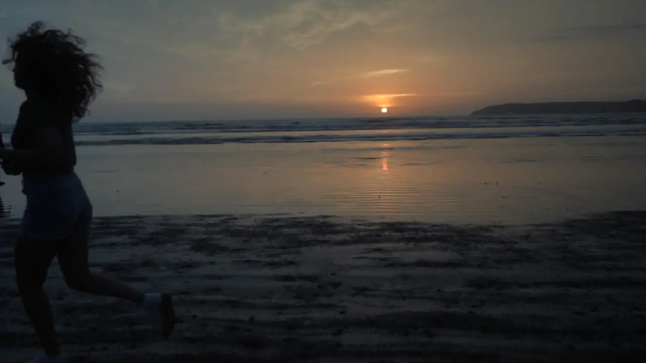 Slow motion landscape view of a young woman silhouette running on a sandy beach by the ocean at sunrise