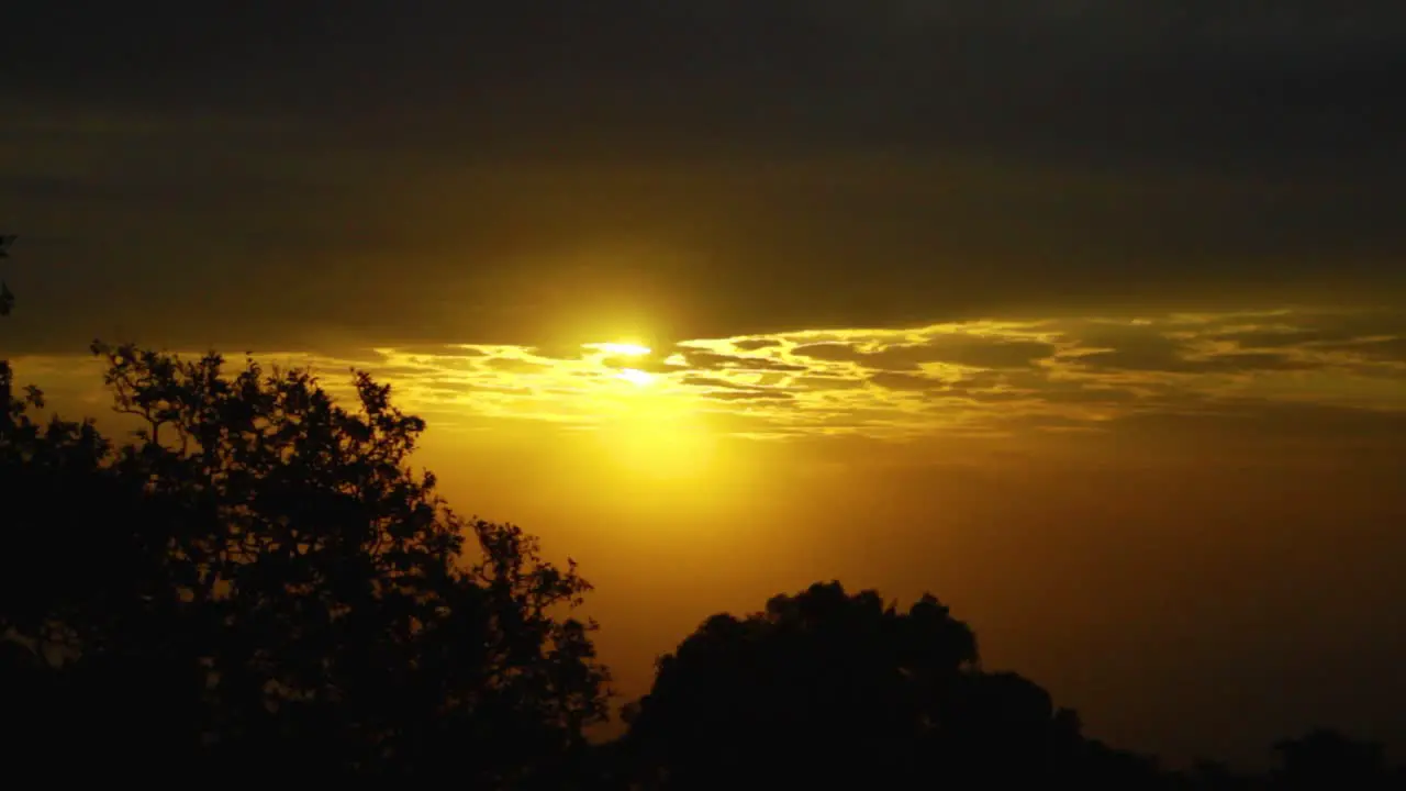 A time-lapse of The Sun going up in an African Plain over a tree covered foreground with cloud cover