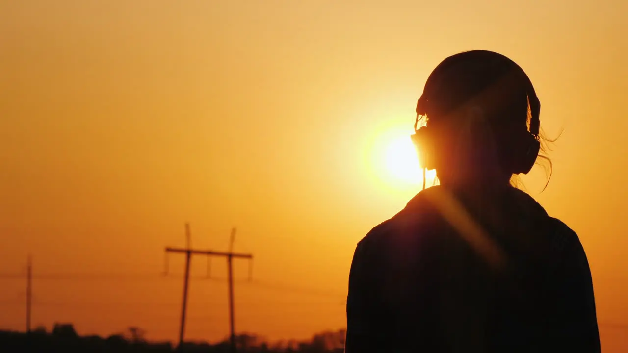 Silhouette Of A Teenager In The Headphones Against The Background Of The City And Sunset