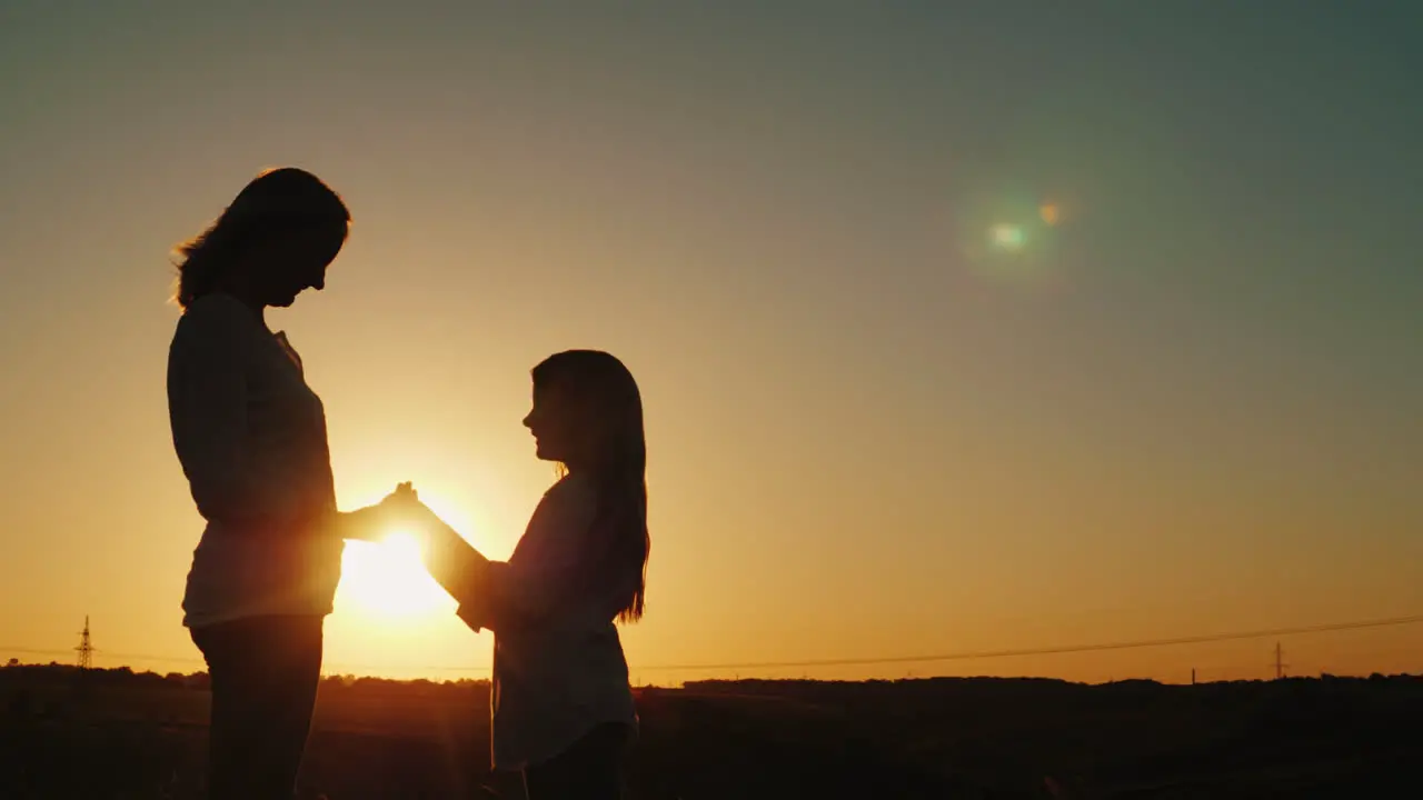 Mom And Daughter Hold Hands Look At Each Other Silhouettes At Sunset 4K Video